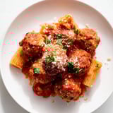 A plate of flavorful turkey meatballs, steaming, piled atop a bed of cooked pasta.