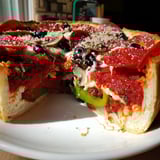 A steaming-hot Deep Dish Pizza, piled with toppings, smells delicious and is perfect for sharing.