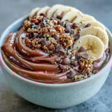 A close-up of a Chunky Monkey Smoothie Bowl with a spoon digging in, revealing rich chocolate and peanut butter flavors.