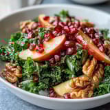 Colorful kale pomegranate bowl featuring juicy seeds, sliced apples, and toasted walnuts, perfect for a healthy vegetarian lunch or side dish.  