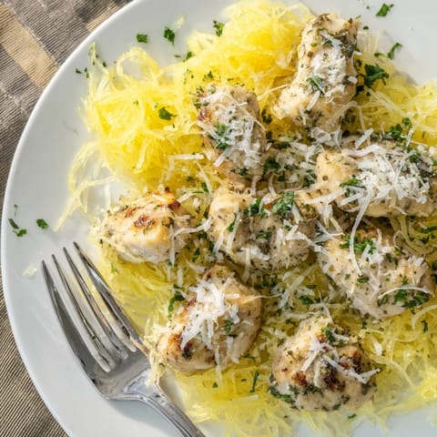A close-up view shows fork-twisted spaghetti squash, savory chicken in lemon sauce, and melted Parmesan cheese.  