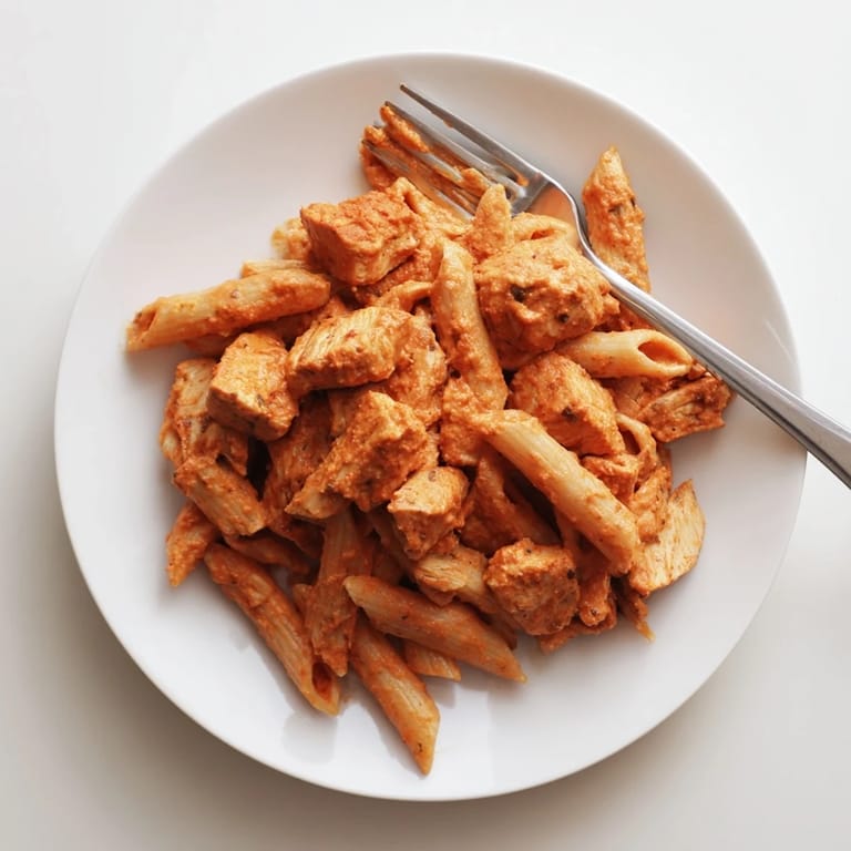 A hearty bowl of Chicken Tikka Pasta, served hot with a swirl of cream and fresh cilantro on top.