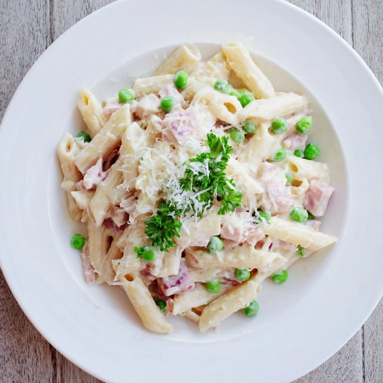 A close-up of Spring Pea & Ham Pasta reveals vibrant green peas, golden ham pieces, and fresh parsley garnish.