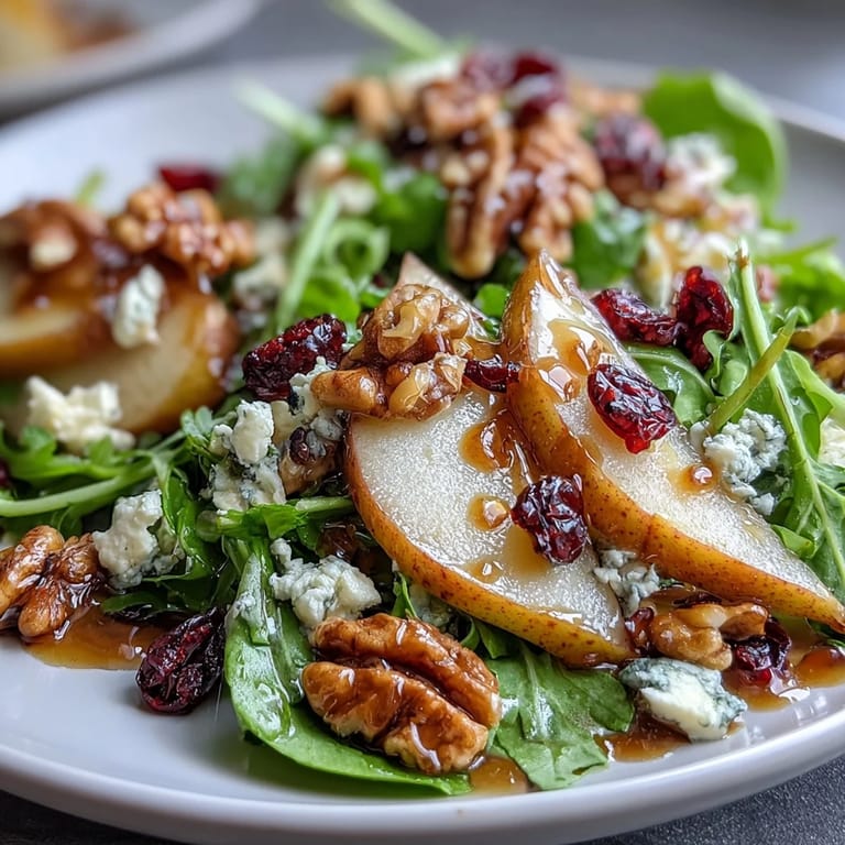 Close-up view of a vibrant Pear Gorgonzola Salad showcasing glistening honey-balsamic dressing, crumbled Gorgonzola, and dried cranberries mixed into crisp spring greens.