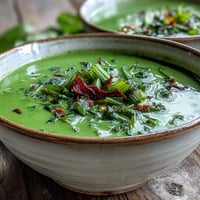 Steaming bowl of Spinach Coriander Lemongrass Soup topped with fresh cilantro and chili slices.
