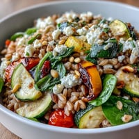 Farro Pasta Bowl with sautéed Mediterranean vegetables, topped with crumbled feta and parsley on a rustic table.