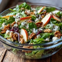 Freshly tossed Mixed Greens and Apple Bowl with crunchy walnuts and creamy goat cheese on a rustic table.